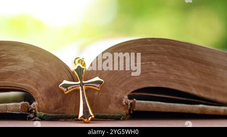 Golden metal cross on an old open book symbolizing the spread of Jesus Christs love among Christians reflecting faith devotion and the importance of C Stock Photo