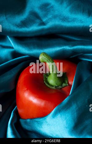 Bright Red Bell Pepper on Deep Teal Satin Background - green fabric covers a pepper Stock Photo