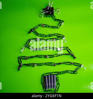 An innovative Christmas tree design crafted using office supplies, like clips and chains, styled artistically against a vibrant green backdrop Stock Photo