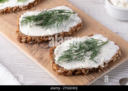 Freshly prepared rye bread topped with creamy spread and dill on a wooden board Stock Photo