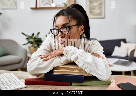 A focused woman rests her chin on books, deep in thought while studying online at home. Stock Photo