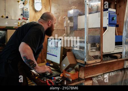 Male engineer operating cutting machine and looking through protective glass while working in plastic recycling workshop Stock Photo