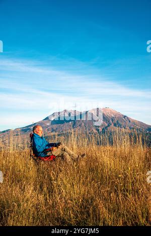 Adult senior male relaxes while reading a kindle book with Mount Saint Helensin the background. Northern Cascades, Washington State. USA Stock Photo