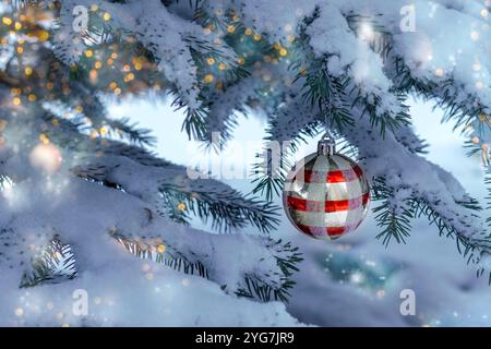 Blue spruce covered in snow and decorated with Christmas red ball and lights. Outdoors on winter day. Postcard. Copy space. Stock Photo
