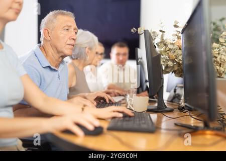 Focused older gentleman using computer at internet cafe Stock Photo