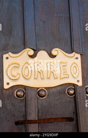 Vertical image of the door of an old post office in the foreground, with the word 'Correo' written in Spanish on a bronze plaque. Stock Photo