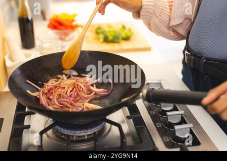 Cooking onions in wok on stove, preparing delicious meal at home kitchen Stock Photo