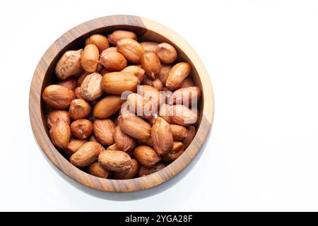 A wooden bowl filled with roasted peanuts is positioned on a white background. The peanuts are brown and plump, with their skins slightly wrinkled. Stock Photo