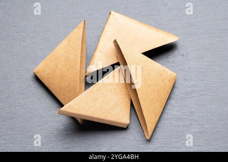 Four brown paper triangles are arranged in a circular pattern on a gray surface. The triangles are slightly overlapping. Stock Photo