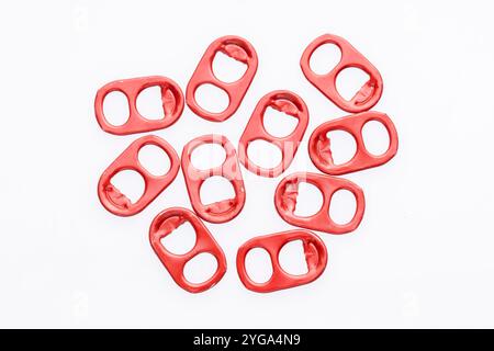 A closeup of ten red metal can pull tabs scattered on a white background. The tabs are slightly worn and have a shiny metallic finish. Stock Photo