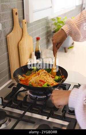 Cooking stir-fry noodles with vegetables on stove in modern kitchen, at home Stock Photo