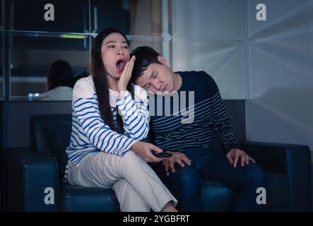 sleepy couple yawning and sleeping while watching TV movie on a sofa at night Stock Photo