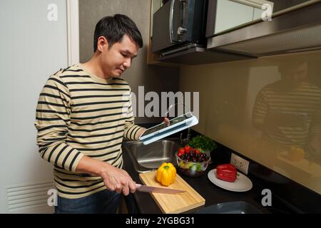 man cooking and preparing food according to a recipe on a tablet computer in the kitchen at home Stock Photo