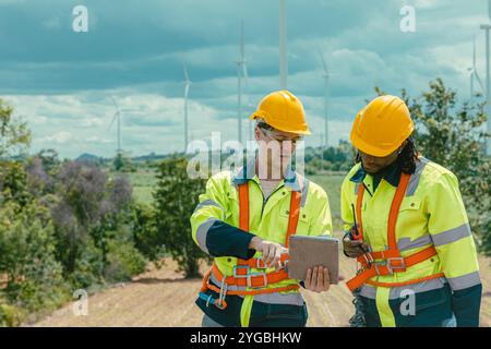 Engineer workers using tablet computer service monitor Wind Turbines status, working survey at wind electricity generator farm field outdoor. Stock Photo