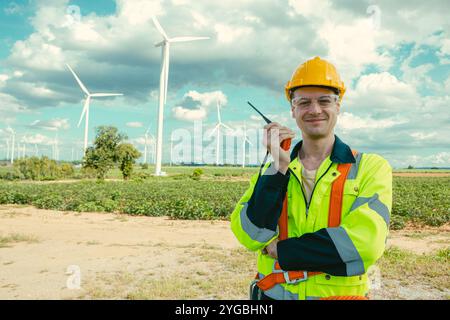 Smart Caucasian Engineer technician male worker standing at Wind Turbines working service manager at wind electricity generator farm field. Stock Photo
