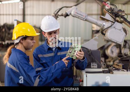 Happy engineer worker team service replace broken part of automatic industry robotic welding arm. Mechanic team repair maintenance robot machine in wo Stock Photo