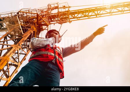 Indian worker engineer construction site control radio operation. Foreman operate tower crane working order by walkie talkie. Stock Photo