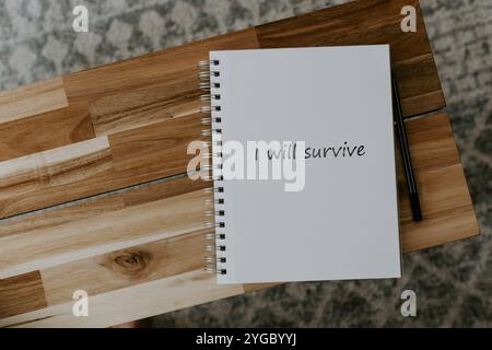 I will survive written on noted pad placed on coffee table alongside a pencil. These are motivational words. Stock Photo