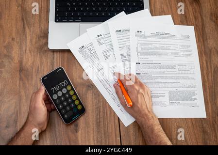 Male entrepreneur engages in filling different tax forms using calculator on modern smartphone Stock Photo
