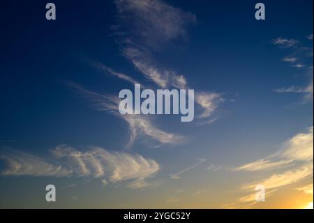 Delicate cloud formations create a mesmerizing pattern against a vibrant evening sky as the sun sets. Stock Photo