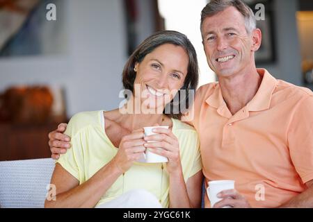 House, portrait and mature couple with coffee, smile and bonding together in living room. Apartment, senior man and woman on sofa, herbal tea or Stock Photo