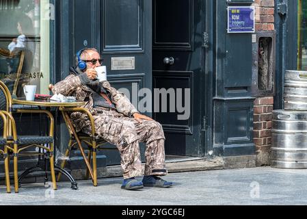 An elderly man wearing headphones and sunglasses enjoys a cup of coffee at an outdoor table of a café in Dublin. Stock Photo