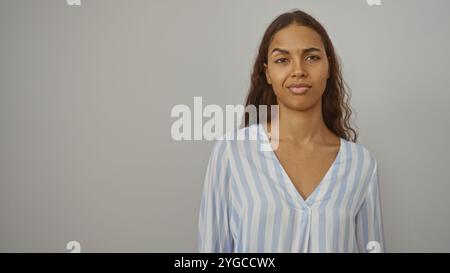 Young woman with a serious expression stands against a plain white background in a studio setting, highlighting her beauty and elegance in a striped s Stock Photo