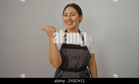 Young hispanic woman wearing apron smiling and pointing to the side over isolated white background Stock Photo