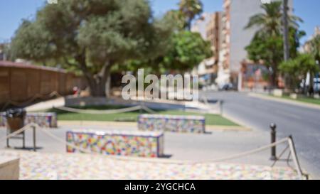 Blurred background of an outdoor public street with colorful benches, trees, and buildings, palm trees lining the road under a bright sunny sky Stock Photo