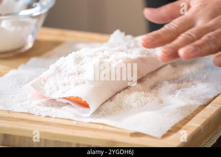 Marinated Salmon with Salt on paper tissue food grade on Wooden cutting plate by Professional hand Chef. Stock Photo