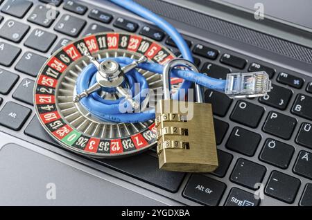 Roulette wheel, padlock and internet cable lying on computer keyboard symbolizing data encryption Stock Photo