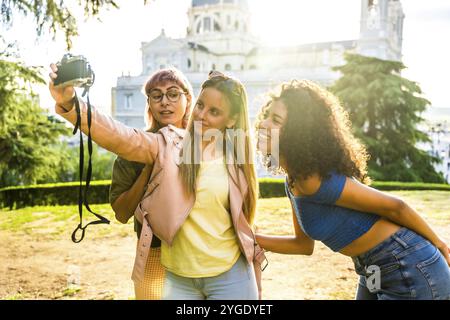 Three female diverse friends taking selfie with camera in a city viewpoint Stock Photo