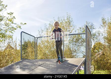 Child on kick scooter in park. Kids learn to skate roller board. Little boy skating on sunny summer day. Outdoor activity for children on safe residen Stock Photo