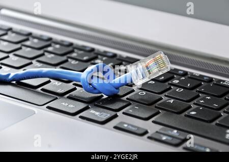 Internet cable with knot on a computer keyboard symbolizing speed or connectivity problems Stock Photo