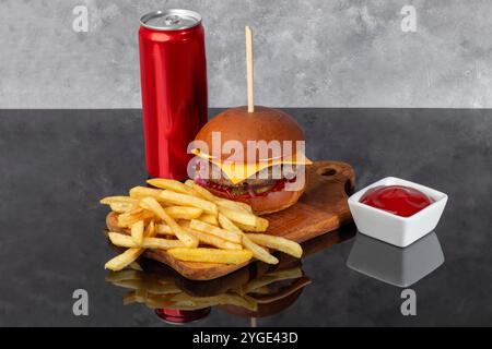 Burger on a wooden board with a patty, tomato, cheese, cucumber and lettuce. Glass of beer in the background. Copy space Stock Photo