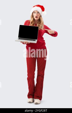 Christmas shopping online, amazed woman in santa hat showing pointing laptop computer blank screen, advertising banner for top offers in sales of Chri Stock Photo