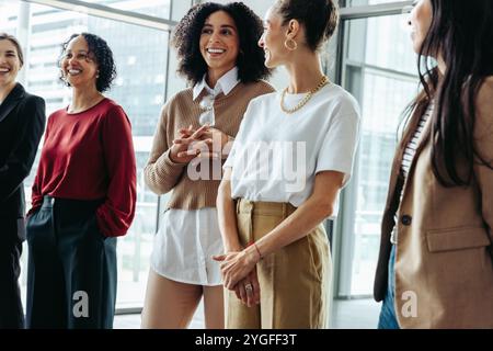 A group of businesswomen engaged in a conversation at a conference, fostering collaboration and teamwork in a modern office setting. Stock Photo