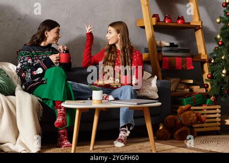 Two friends in cheerful sweaters relax together, sipping warm drinks and celebrating the festive season. Stock Photo
