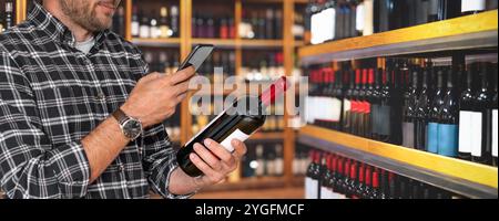 Male customer in wine shop holding wine bottle and scanning e-label using smartphone. Stock Photo