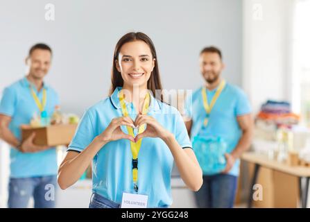 Young happy woman volunteer making heart gesture volunteering in charitable foundation Stock Photo