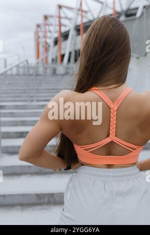 the back of a woman wearing an orange sports bra and white shorts is shown Stock Photo