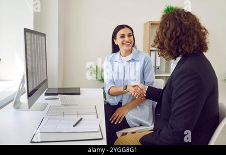 Business people sitting in office on workplace making a deal. Man shaking hand with woman. Stock Photo