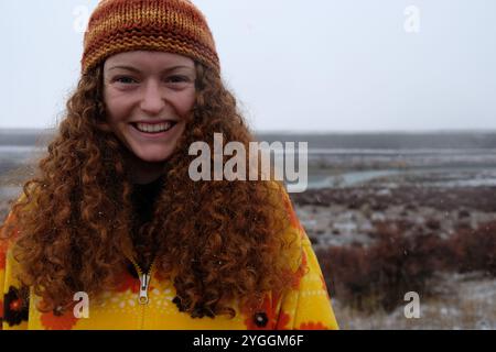 Curly redhead woman stands with snowflakes in her hair, smiling amidst snowfall in Tekapo, South Island, New Zealand Stock Photo