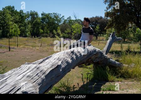 young man sitting on tree trunk in nature Stock Photo