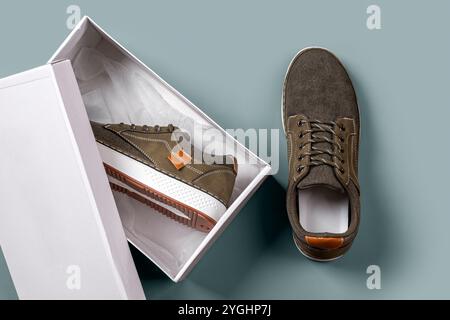 Khaki canvas sneakers in a box against silver blue background. Pair of brown textile shoes with white soles for fitting. Comfortable new sneakers. Stock Photo