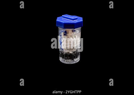 A small container of contact lens solution sits on a table next to a contact lens case and a contact lens Stock Photo