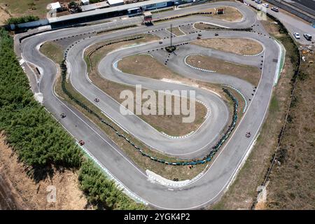 Drone capturing go-karts moving on winding race tracks from top aerial perspective. Distant view of racing competition on road at countryside during daytime.  Stock Photo