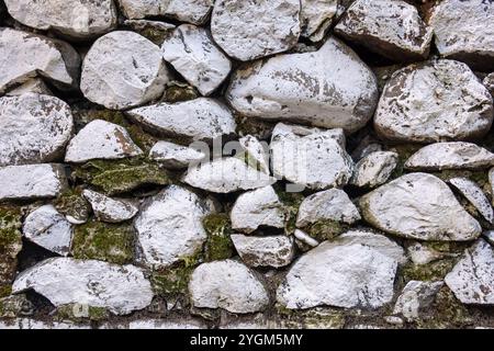 A close-up of a stone wall composed of irregularly shaped, white stones with patches of moss and dirt. The stones are stacked tightly. Stock Photo