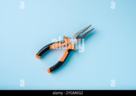 Orange and black handled needle nose pliers on a blue background Stock Photo