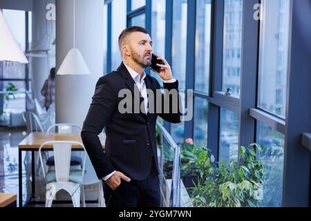 Adult male businessman, teacher, mentor looks out the large window of his office. Work in the office. Development of a new business project Stock Photo